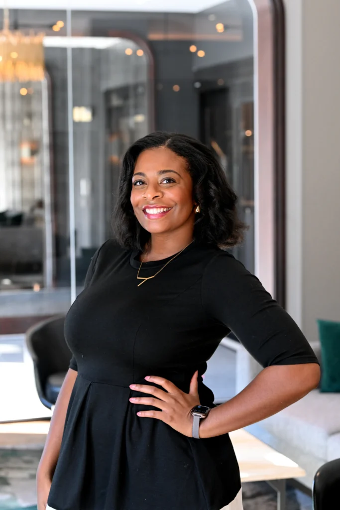 Yasmine Ali, Executive at Director SalivaDirect Inc. standing in an office wearing a black dress with her hand on her hip.