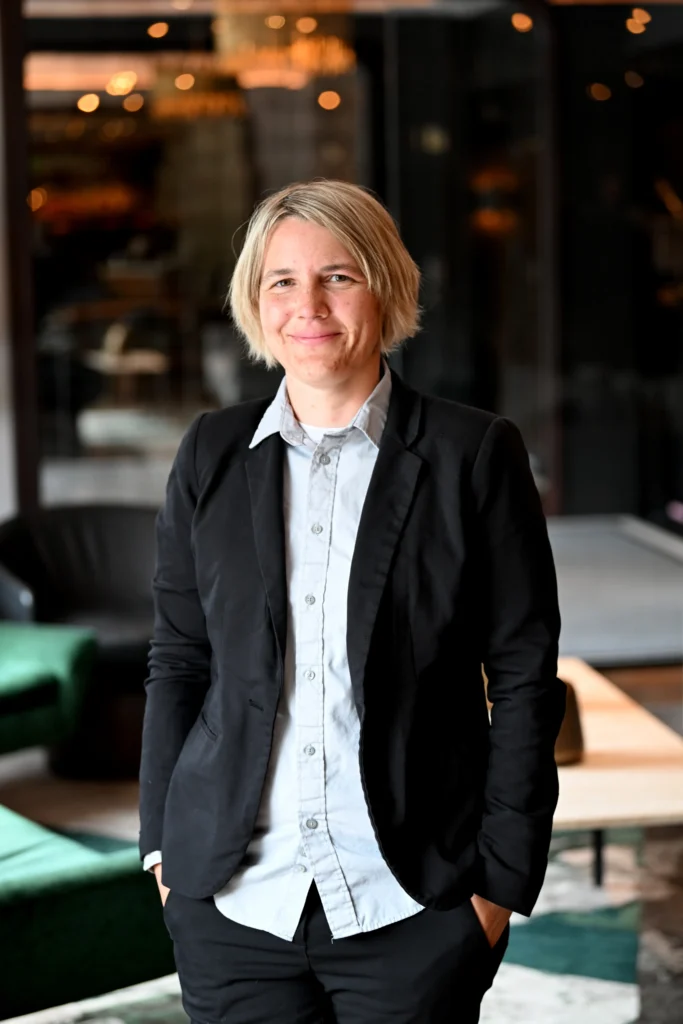 Alexandra Kitz, Director of Science at SalivaDirect Inc. standing wearing a black blazer, with a light blue shirt. Her hands are in her pockets.