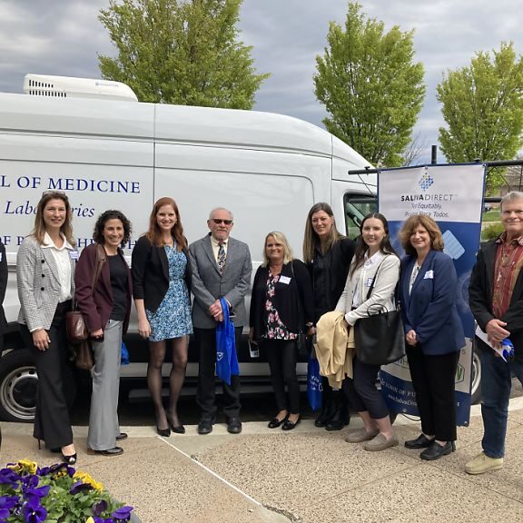SalivaDirect Inc team (one man and seven woman) standing beside the SalivaDirect mobile van.