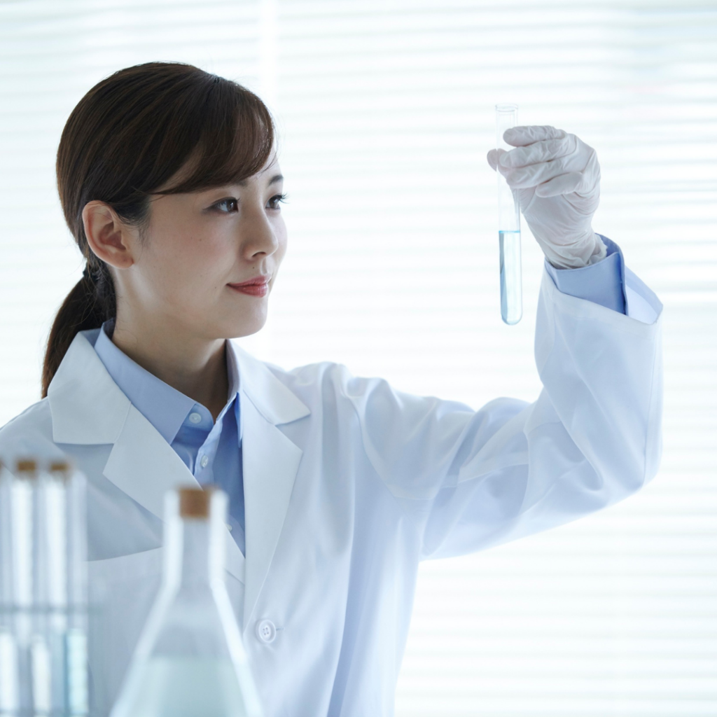 A woman scientist wearing a white labcoat and white gloves holding a test tube up to eye level